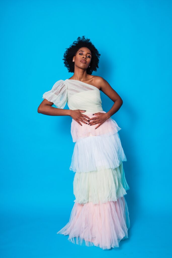 Elle Friberg wearing a long pastel dress in front of blue background